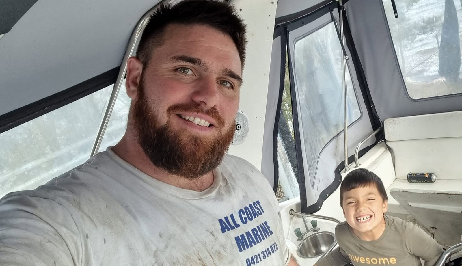 Aaron in his All Coast Marine shirt on board a boat, with a young offsider grinning beside him